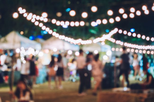 Grünes Eventmanagement - Unscharfes Bild eines belebten Outdoor-Events bei Nacht, beleuchtet von Lichterketten, was eine festliche und gemütliche Atmosphäre schafft.