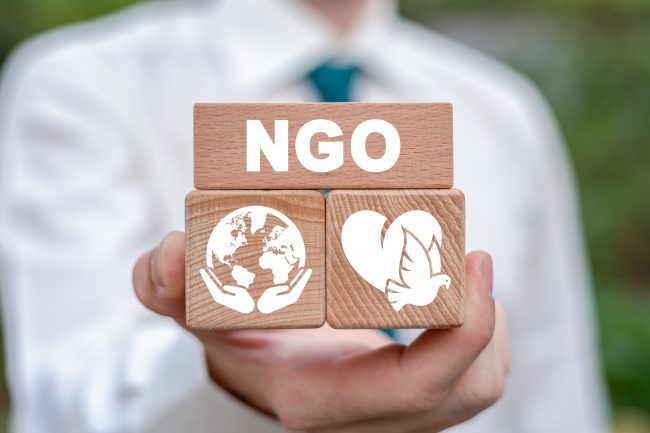 Hände in weißem Laborkittel halten hölzerne Blöcke mit den Buchstaben "NGO" und Symbolen für den Weltfrieden und das Herz.