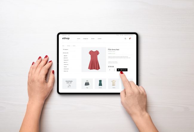 Nachhaltigkeit E-Commerce - Hände einer Person, die auf einem Tablet einen roten Kleid online in einem E-Commerce-Shop zum Warenkorb hinzufügt.