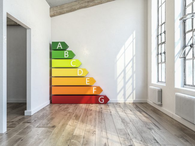 Ein leeres Zimmer mit Energieeffizienz-Bewertungsskala in Form von farbigen Stufen, die von Grün für 'A' bis Rot für 'G' reichen, symbolisiert die Energieeffizienz eines Gebäudes.